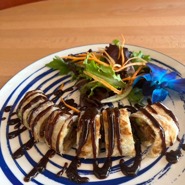 Sliced Thai roti with dark sauce drizzle, side salad, and a blue orchid on a striped plate.