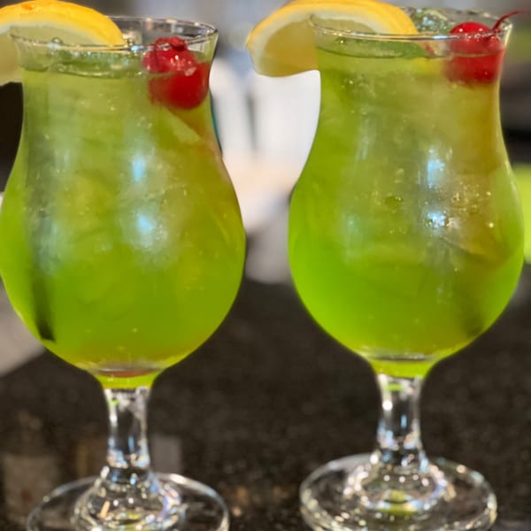 Two vibrant green Sala Thai cocktails with lemon slices and cherries on a dark surface.