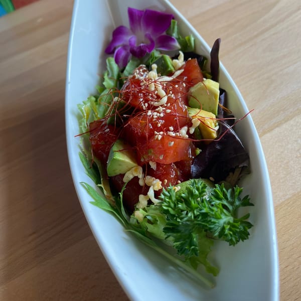 A Thai tuna poke salad with avocado, sesame seeds, and chili threads in a white boat-shaped dish.