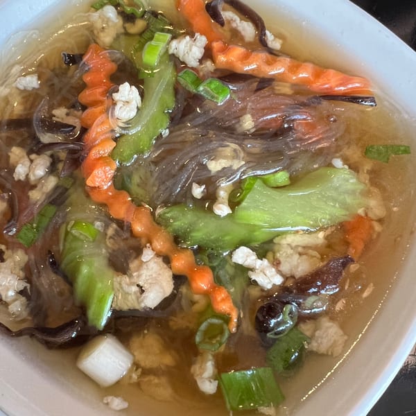 Close-up of a Thai glass noodle soup with minced pork, carrots, and green vegetables.