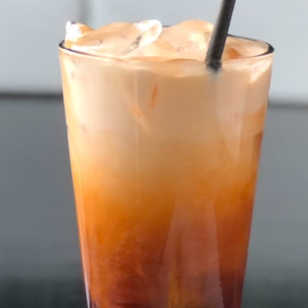 A tall glass of Sala Thai iced tea with ice and a black straw.