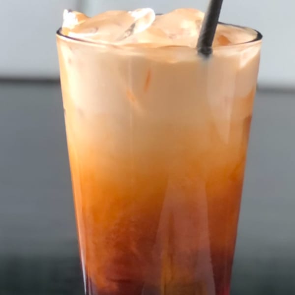 A tall glass of Sala Thai's iced Thai tea with a black straw and ice.