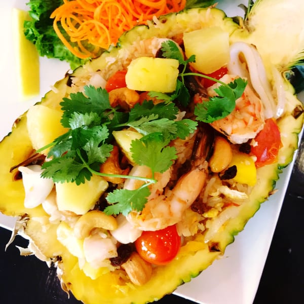 Pineapple fried rice with shrimp, squid, cashews, and cilantro served in a pineapple half.