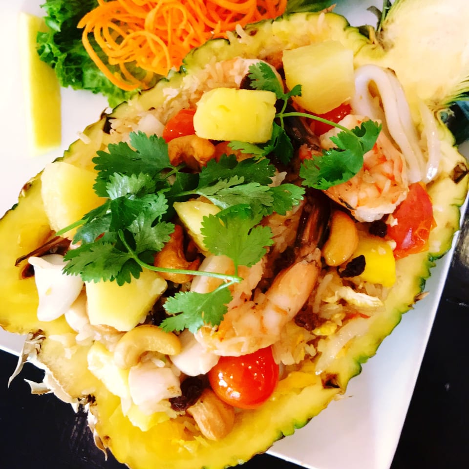 Pineapple fried rice with shrimp, squid, cashews, and cilantro served in a pineapple half.
