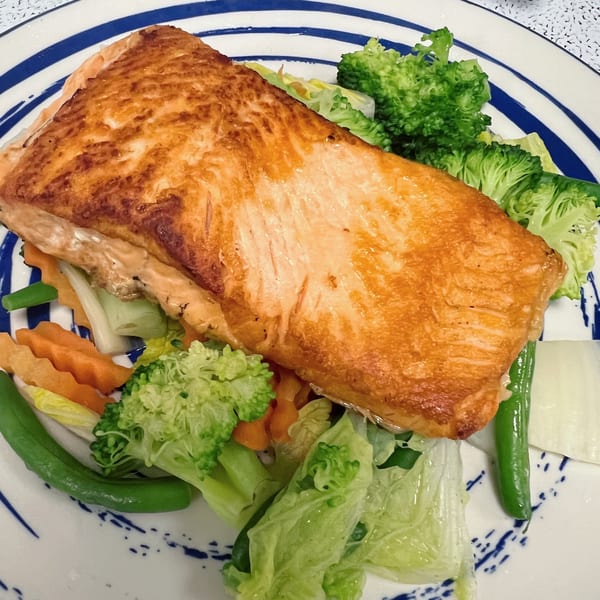 Crispy pan-seared salmon fillet served with steamed broccoli, carrots, green beans, and lettuce on a striped plate.