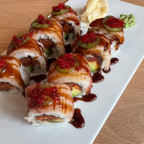 Sushi rolls topped with red caviar, green jalapeños, and a sweet brown sauce on a white plate.