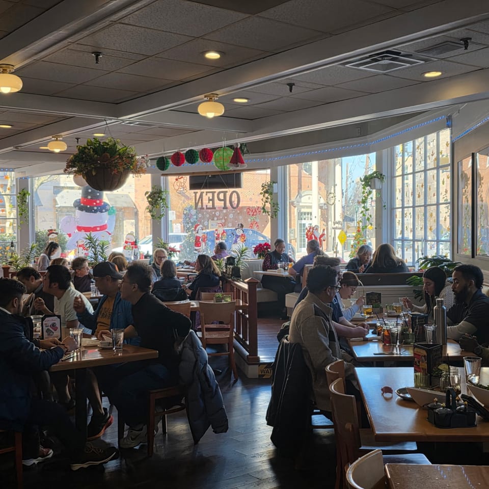 A busy Sala Thai dining room with patrons seated at tables and large windows decorated for holidays.