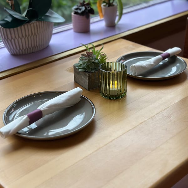 A wooden table set for two with gray plates, white napkins, a succulent, and a lit candle.