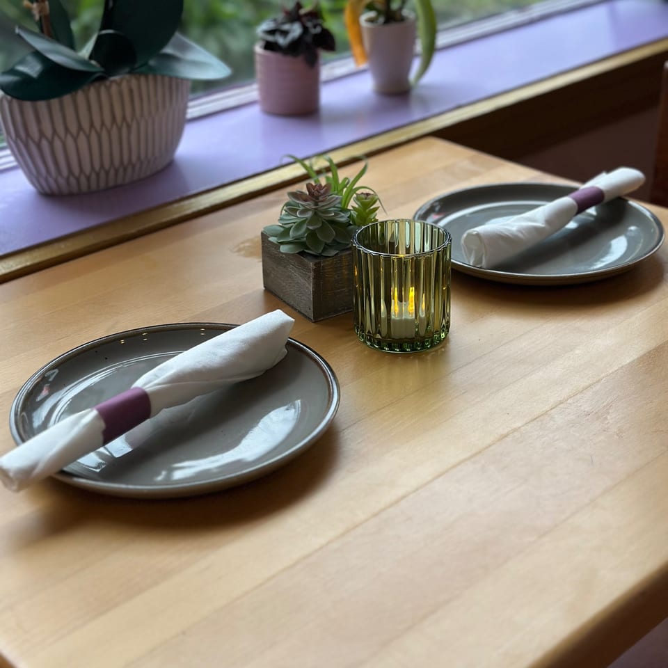 A wooden table set for two with gray plates, white napkins, a succulent, and a lit candle.