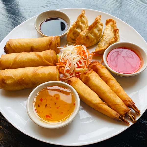 A white plate with Sala Thai's fried spring rolls, dumplings, and shrimp rolls, served with dipping sauces.