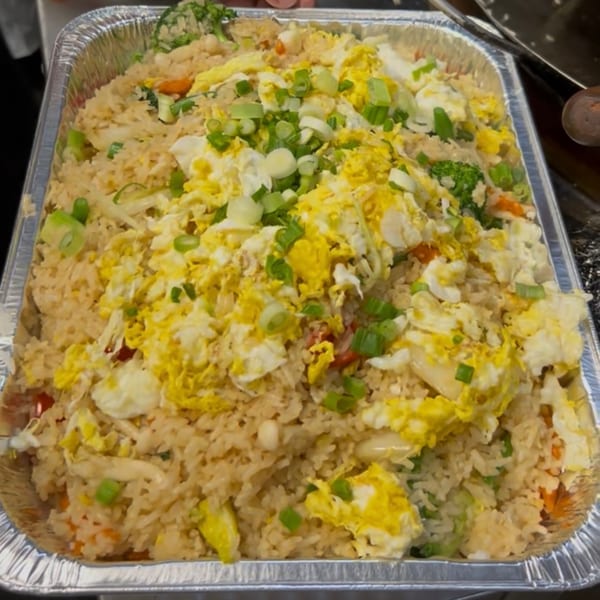 A large foil tray filled with Sala Thai's fried rice, topped with scrambled egg and green onions.