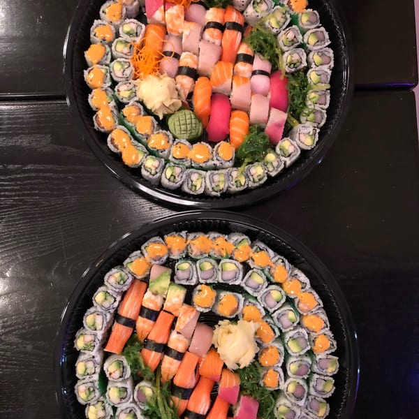Two large platters of assorted Sala Thai sushi rolls and sashimi on a dark table.