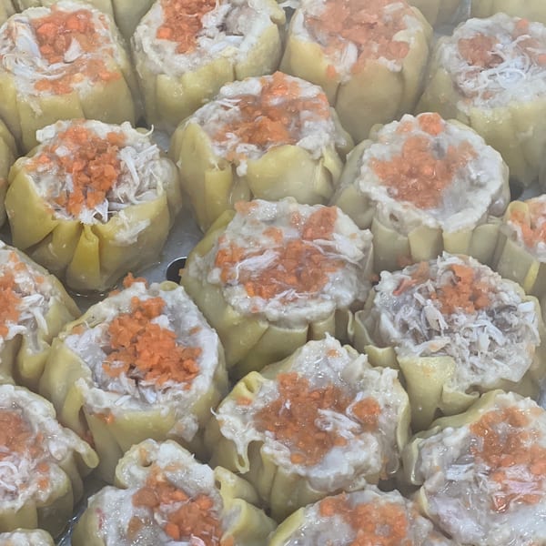 Close-up of numerous steamed Sala Thai dumplings, topped with shredded crab meat and orange roe.