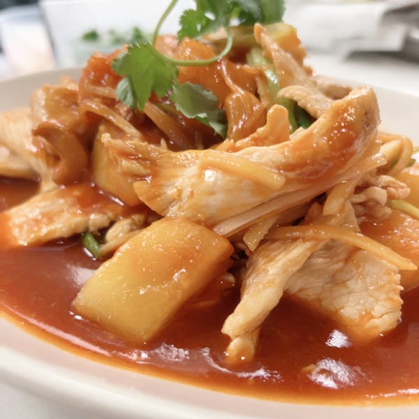 Sweet and sour chicken with pineapple and cilantro in a red sauce on a white plate.