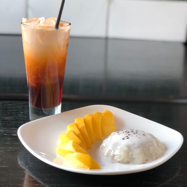 Thai iced tea and mango sticky rice with coconut milk and sesame seeds on a white plate.