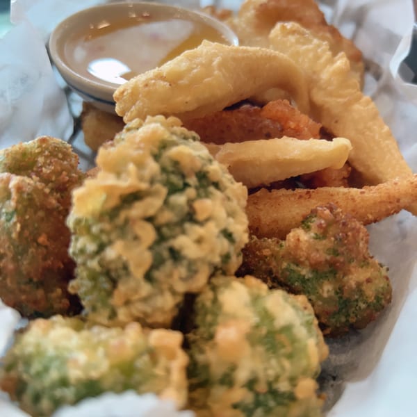 Crispy fried broccoli and other vegetables with a small bowl of dipping sauce in a white basket.