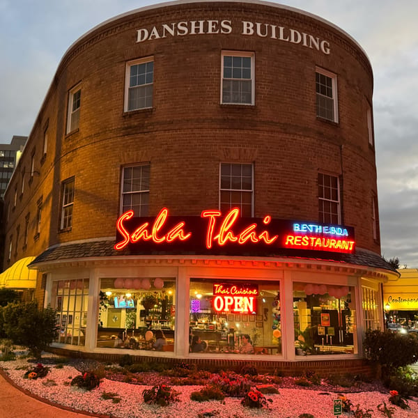Sala Thai restaurant exterior at dusk, with a bright neon sign and visible interior through large windows.