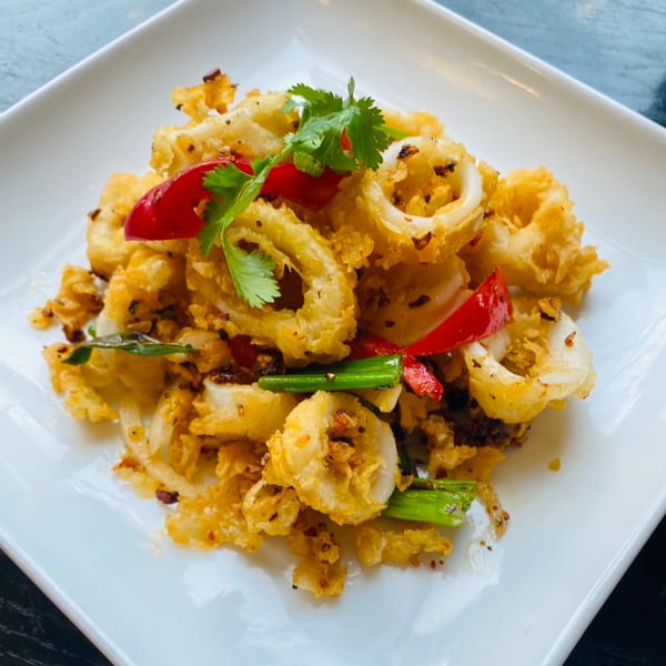 Crispy fried calamari rings with red bell peppers, green onions, and cilantro on a white plate.