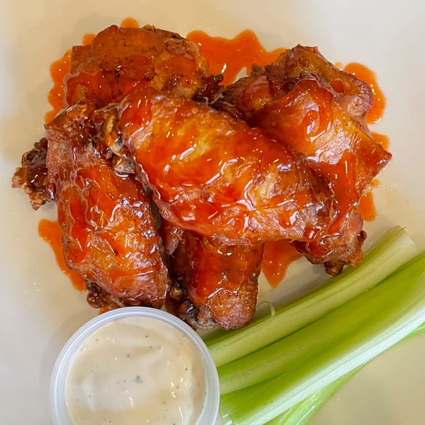 Sweet chili chicken wings with celery sticks and ranch dressing on a white plate.