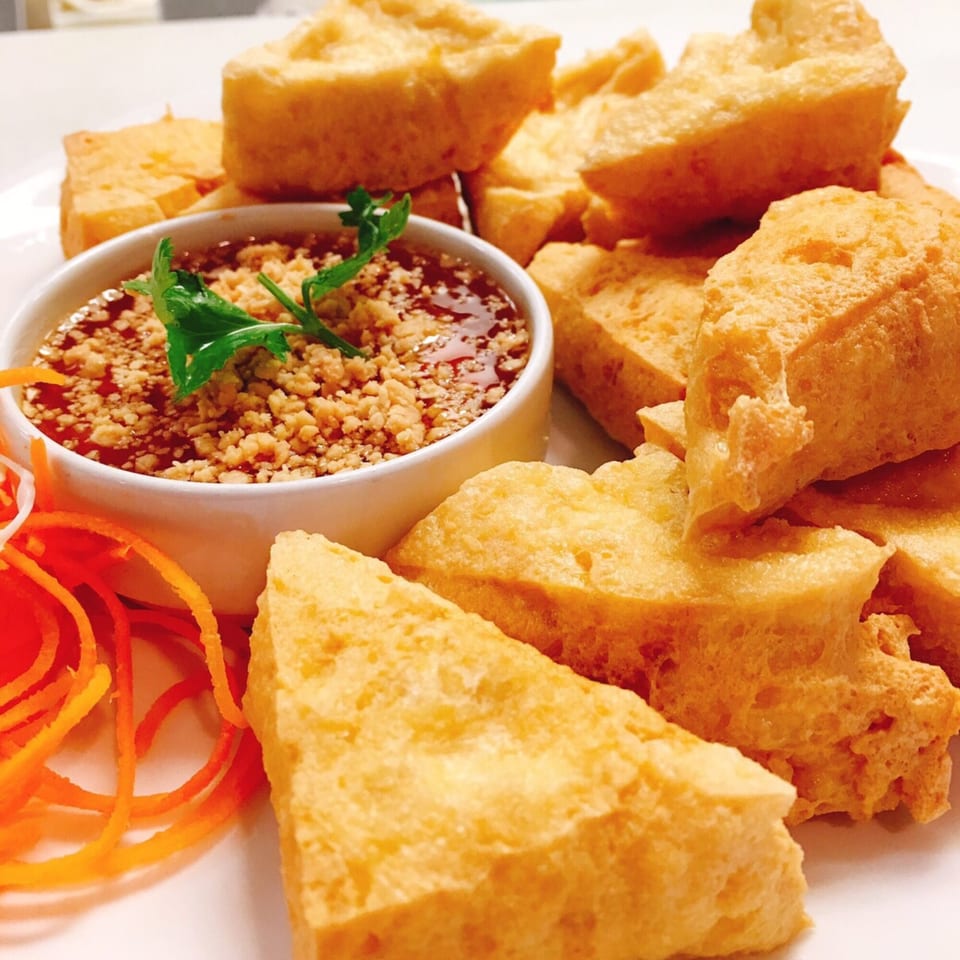Golden fried tofu pieces arranged around a small bowl of dipping sauce with peanuts and cilantro.