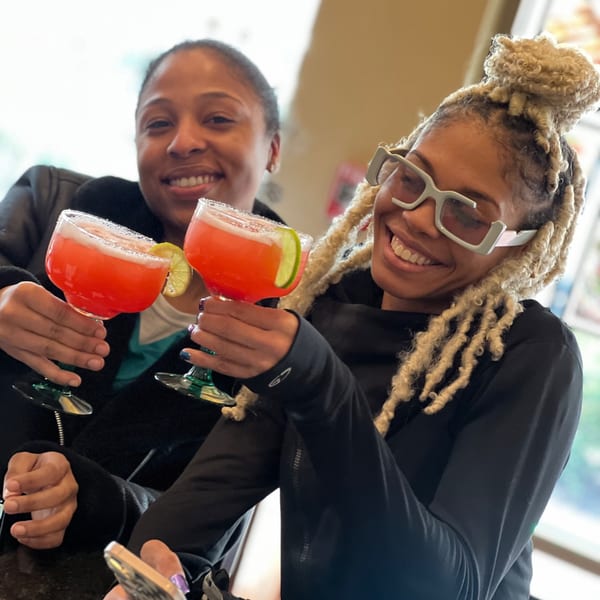Two women smiling and holding up red margaritas with lime wedges and salt rims.