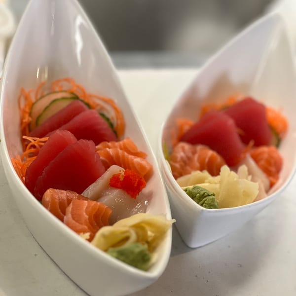 Two white boat-shaped bowls filled with colorful sashimi, ginger, and wasabi.