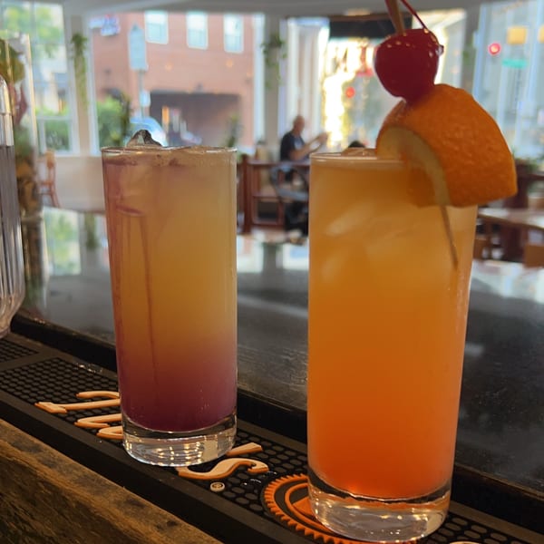 Two colorful Sala Thai cocktails on a bar, one garnished with an orange slice and cherry.