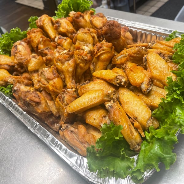 A large catering tray filled with golden-brown Sala Thai chicken wings and fresh green lettuce.