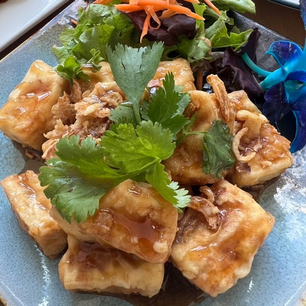 Crispy fried tofu pieces drizzled with sauce, garnished with cilantro, lettuce, and shredded carrots.