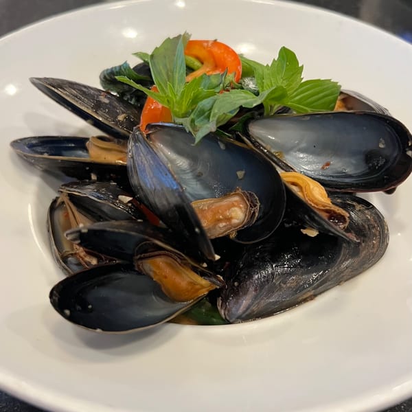 Steamed mussels in a white bowl, garnished with fresh basil and red bell pepper.