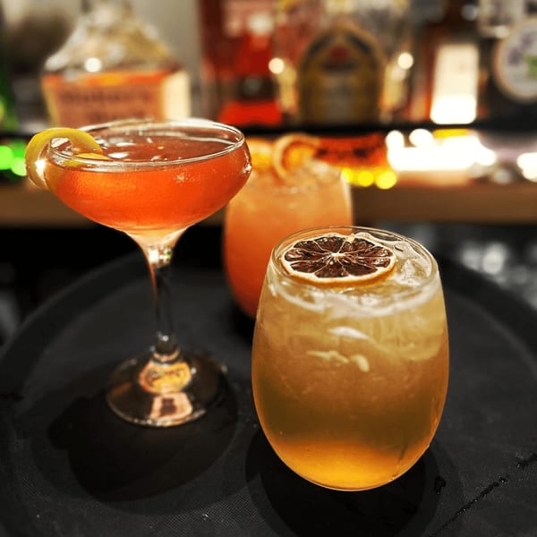 Three vibrant Sala Thai cocktails, two garnished with citrus, on a dark tray in a dimly lit bar.