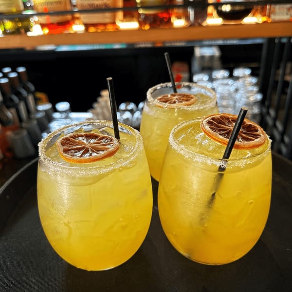 Three Sala Thai margaritas with salted rims, dried orange slices, and black straws on a tray.