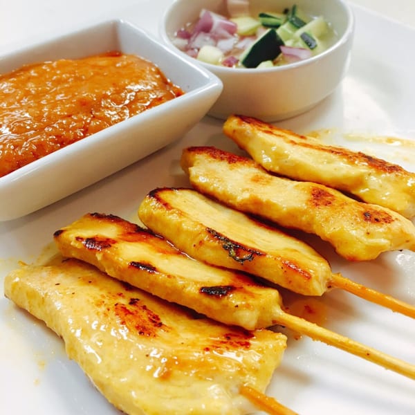 Grilled chicken satay skewers with peanut sauce and a side of cucumber relish.