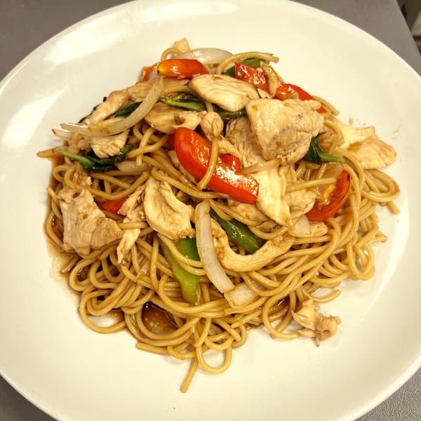 Sala Thai's chicken Pad See Ew with wide noodles, red bell peppers, and onions on a white plate.