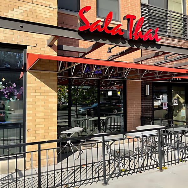 Exterior of Sala Thai restaurant with a red awning, outdoor seating, and a brick facade.