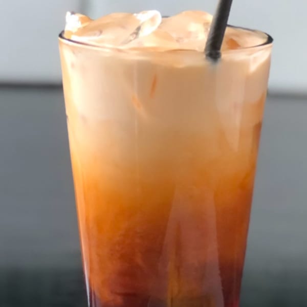 A tall glass of Sala Thai iced tea with ice and a black straw.