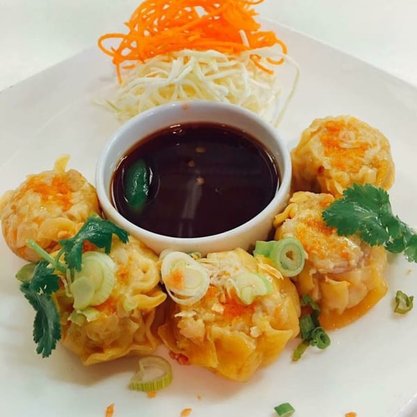 Sala Thai's steamed dumplings with a dark dipping sauce, garnished with cilantro and scallions.