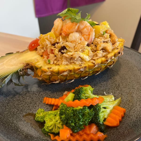 Pineapple fried rice with shrimp and cashews, served in a pineapple half with a side of broccoli and carrots.